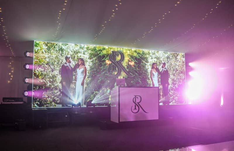 A couple on screen above a wedding dancefloor at a fusion celebration