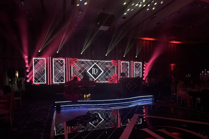 The finished stage on the night: LED panels with the monogram, beams, DJ booth and curved LED-edged riser