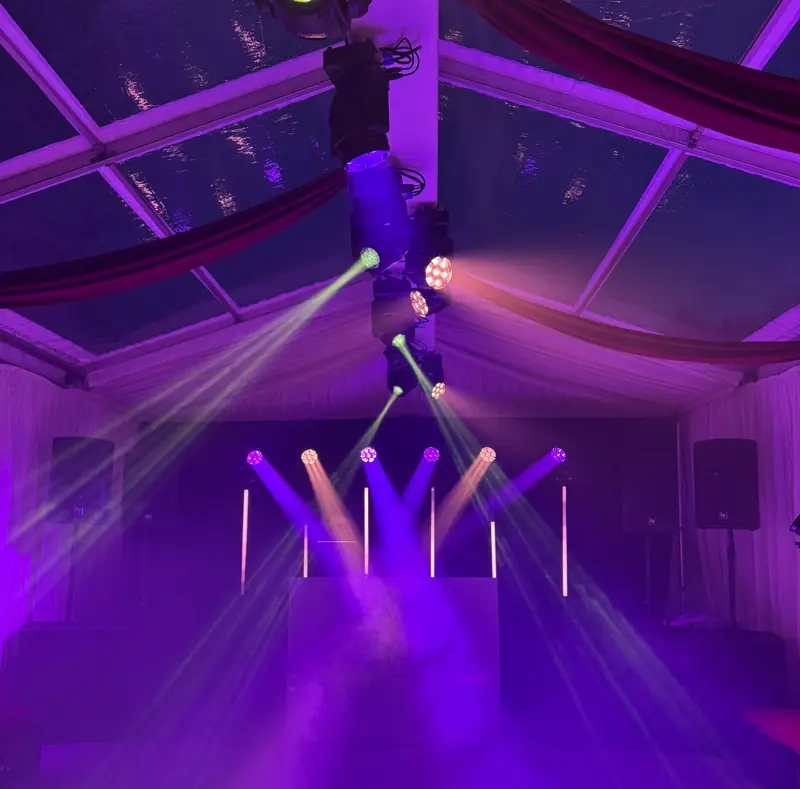 Purple moving-head beams crossing a marquee from a rigged truss